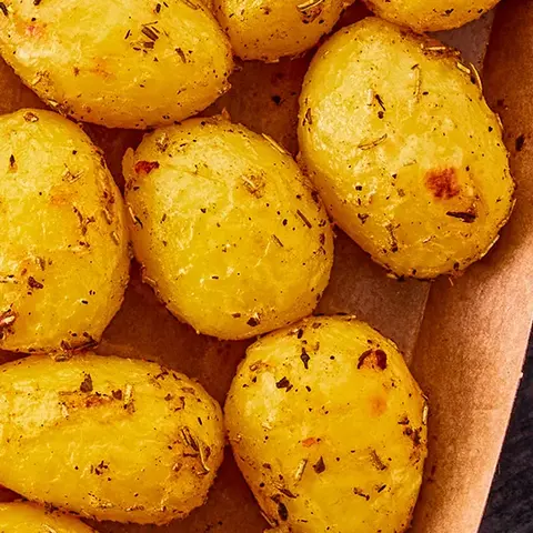 Rosmarinkartoffeln in einer Backschale, serviert mit einem frischen grünen Salat, getoppt mit karamellisiertem Honig-Ziegenkäse und Walnüssen, angerichtet auf einem dunklen Servierbrett mit blauer Stoffserviette und schwarzem Besteck.